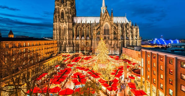 Christmas Market stalls with red roofs and white lights sit in front of the Cologne Cathedral