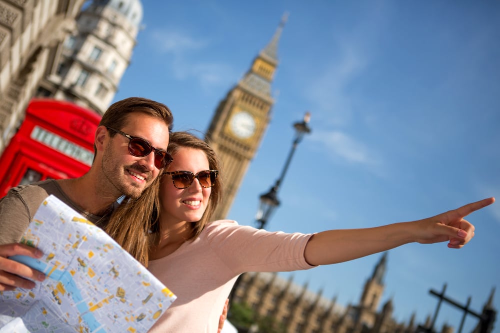 Couple of tourists in London holding a map. A red phone booth is behind them 