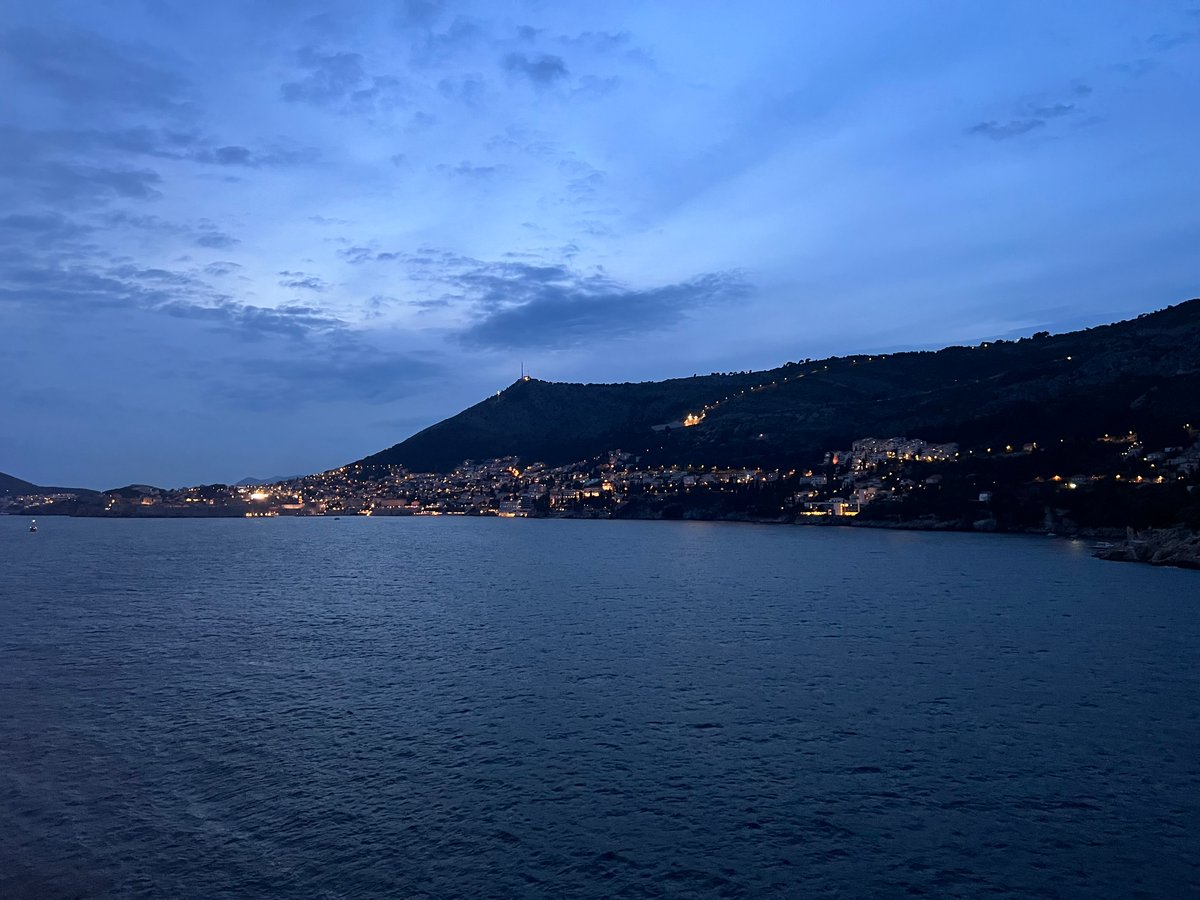 A view of Old Town Dubrovnik at night. The bay is in the foreground and you can see lights on the mountainside in the background